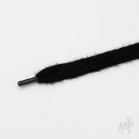 Close-up of a soft, fuzzy black cashmere shoelace with a black aglet on a white background.