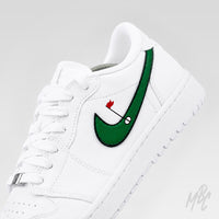 Close-up of a white Air Jordan 1 Low Golf shoe highlighting the green, black-outlined Nike Swoosh with a red flag and golf-hole graphic.
