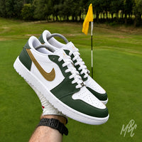 Pair of Fairway Gold custom Jordan 1 Low Golf shoes with hand-painted green and gold colour blocking, held above a golf green beside the pin.