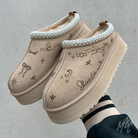 Beige UGG Tazz II slippers with decorative patterns on a gray background