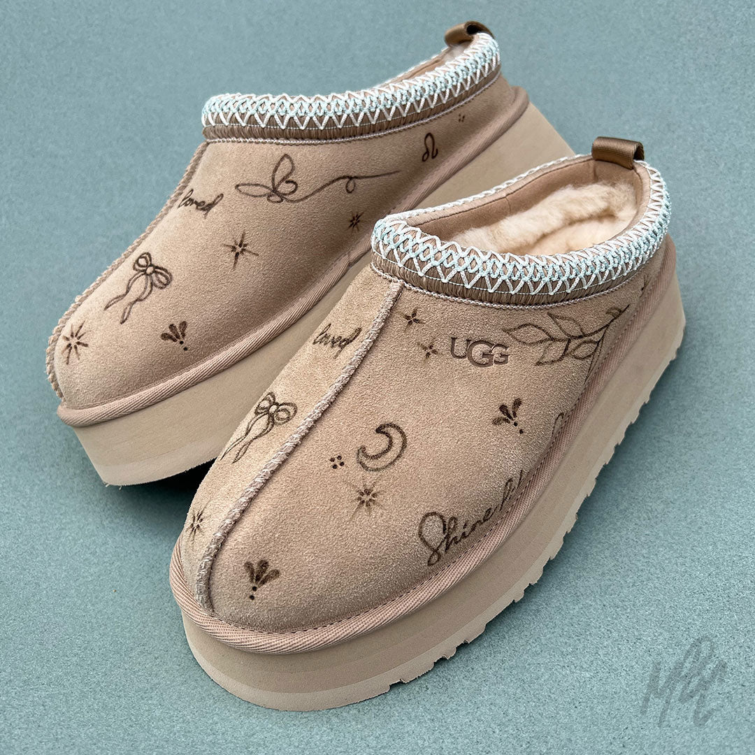 Pair of beige UGG Tazz II slippers with pyrography burnt onto the suede