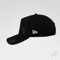 Side profile of the Midnight Canvas custom New Era cap featuring distressed white embroidered LA logo, hand-painted blue paint splatters and a black curved-brim design.
