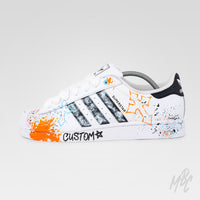 Outside view of Modern Relic custom Adidas Superstar featuring textured black painted stripes, graffiti-inspired graphics, orange and blue paint splatters and hand-painted details.