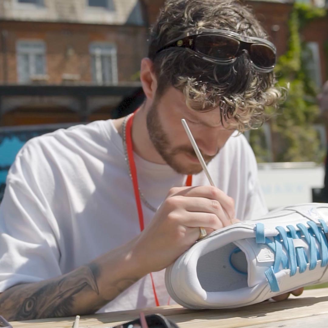 An artist hand painting custom puma trainers for the soccer aid players