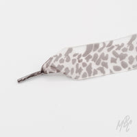 Close-up of a wide white ribbon shoelace with a gray snow leopard print and matching aglet on a white background.