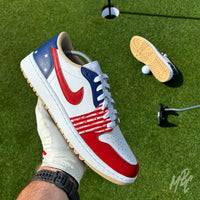 Stateside Drive custom Jordan 1 Low Golf shoes with hand-painted USA-inspired detailing, photographed on a golf course putting green beside the hole and flag.