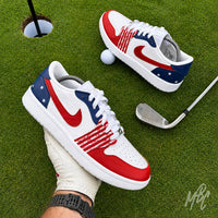 Stateside Drive custom Jordan 1 Low Golf shoes held above a putting green, featuring hand-painted patriotic red, white and blue with a golf club and golf ball.