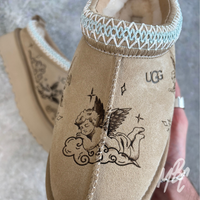 Detailed view of hand-engraved cherub illustration on suede UGG Tazz II, showcasing permanent etched artwork
