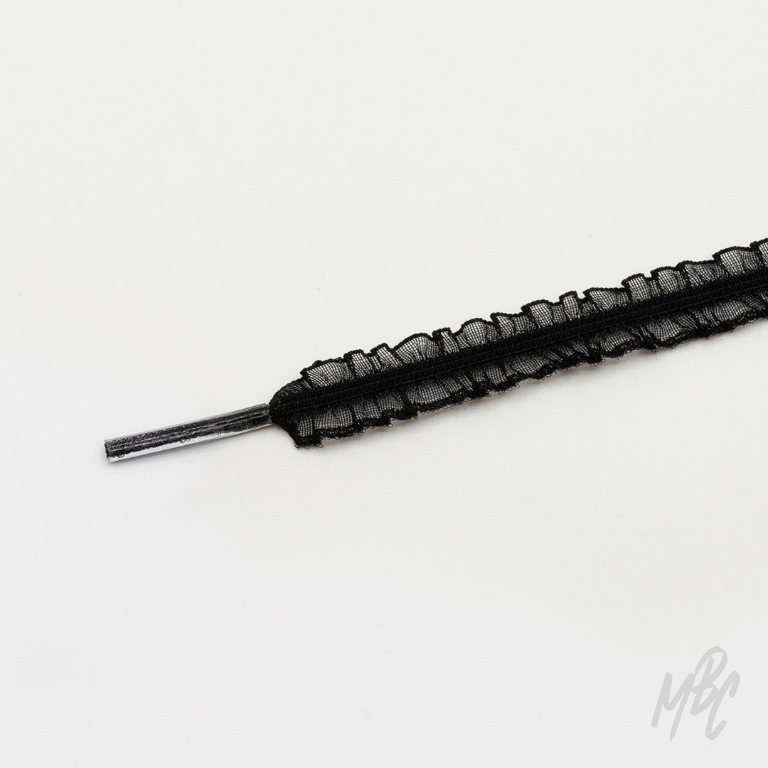 Close-up of a black mesh shoelace with ruffled edges and a clear plastic aglet on a white background.