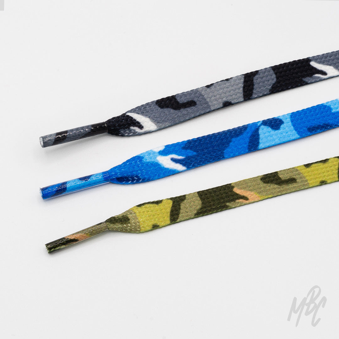 Three flat camouflage shoelaces in grey, blue, and green with matching patterned aglets, arranged on a white background.