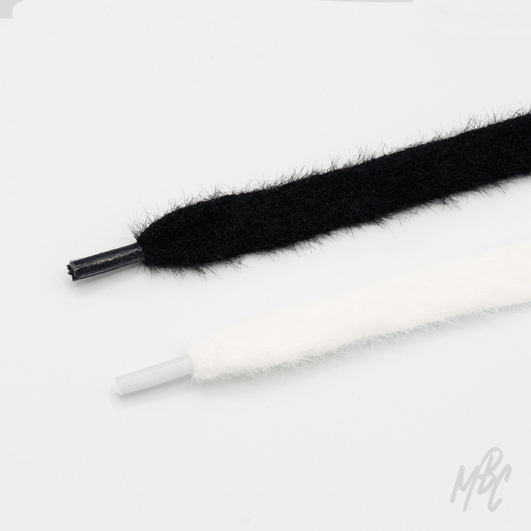 Close-up of black and white fuzzy cashmere shoelaces with matching aglets arranged on a white background.