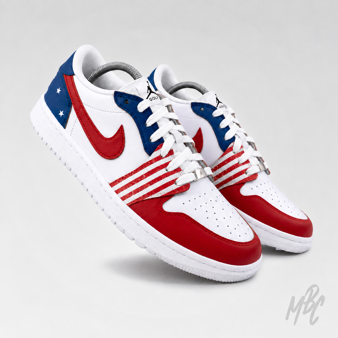 A pair of Nike Air Jordan 1 Low sneakers styled with an American flag theme, featuring a white leather base with red overlays on the toe, quarter, and Swoosh, and a blue star-patterned heel tab. The shoes are displayed against a light gray studio background.