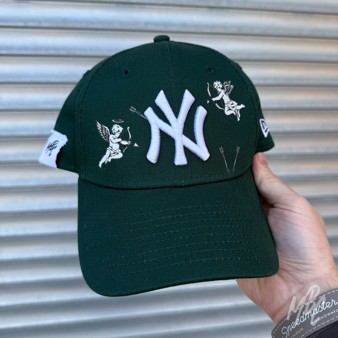 Green New Era NY custom cap with cherub cupid illustrations and white embroidered logo shown in lifestyle shot