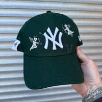 Green New Era NY custom cap with cherub cupid illustrations and white embroidered logo shown in lifestyle shot
