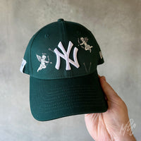 Cherub New Era NY custom cap in green with cupid angel graphics and embroidered NY logo held in hand