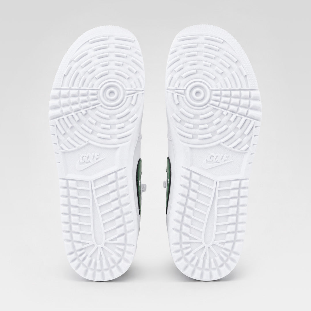 Bottom view of a pair of white Air Jordan 1 Low Golf shoes, showing the circular traction pattern and Nike Golf branding on the outsoles.
