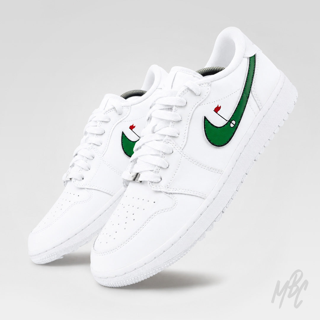 Angled studio view of a pair of white Air Jordan 1 Low Golf shoes with green, black-outlined Swooshes featuring red golf flags.