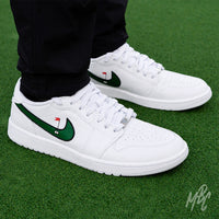 Close-up of white Air Jordan 1 Low Golf shoes with green golf-themed Swooshes worn with black trousers on a putting green.