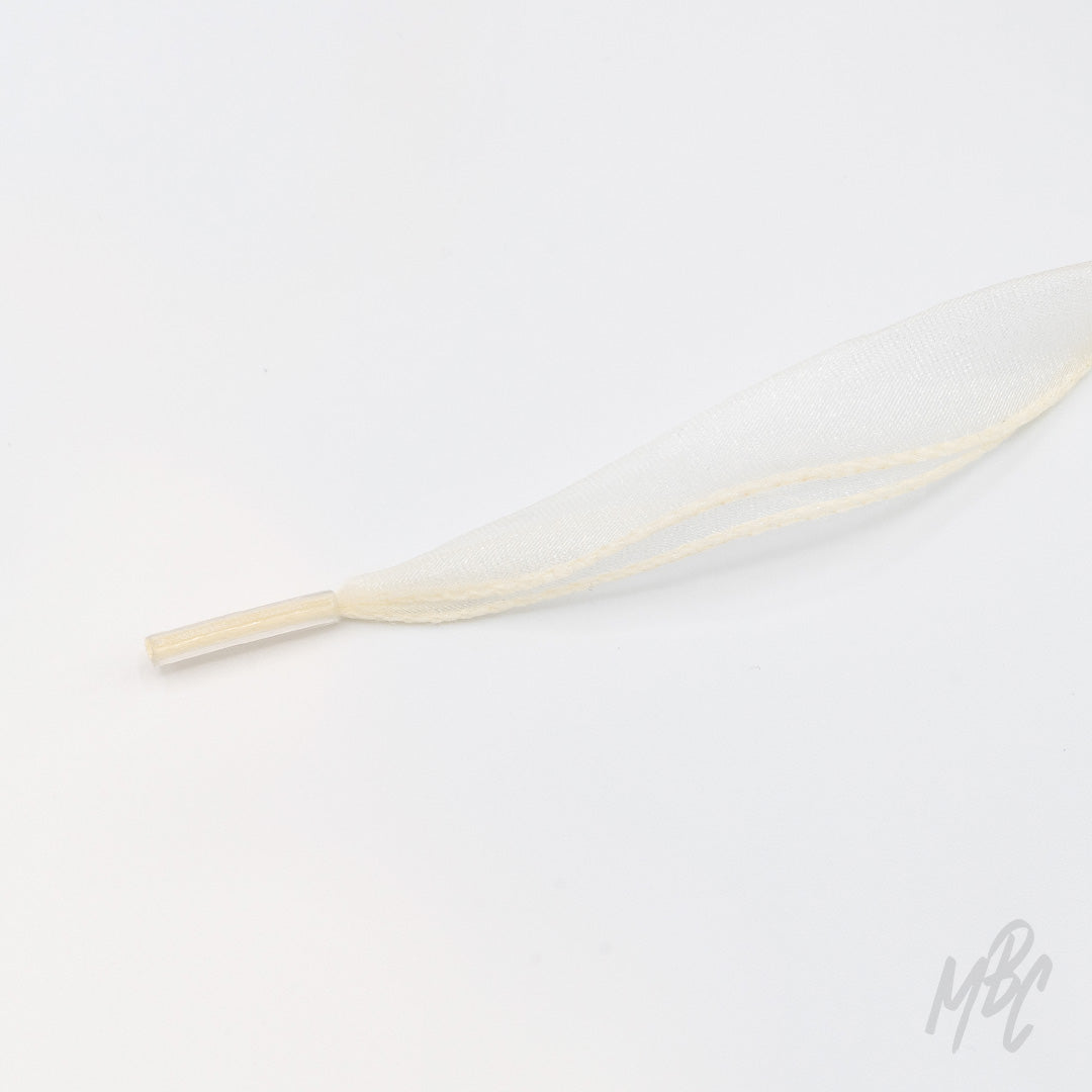 Close-up of a cream fishtail ribbon shoelace with a clear plastic aglet on a white background.