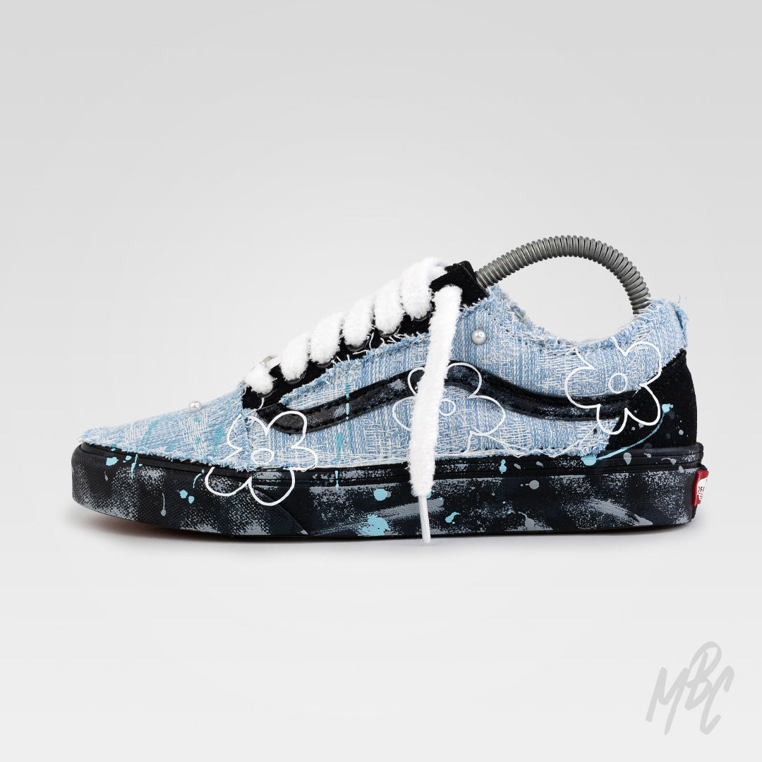 Side view of custom Denim Bloom Vans Old Skool with distressed denim upper, white floral graphics, fluffy white laces and paint-splattered black midsoles.