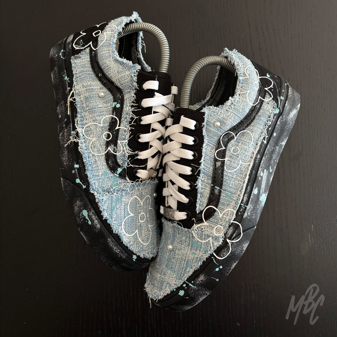 Top-down view of Denim Bloom custom Vans Old Skool sneakers with distressed denim, white flower artwork, paint-splattered midsoles and fluffy white laces.