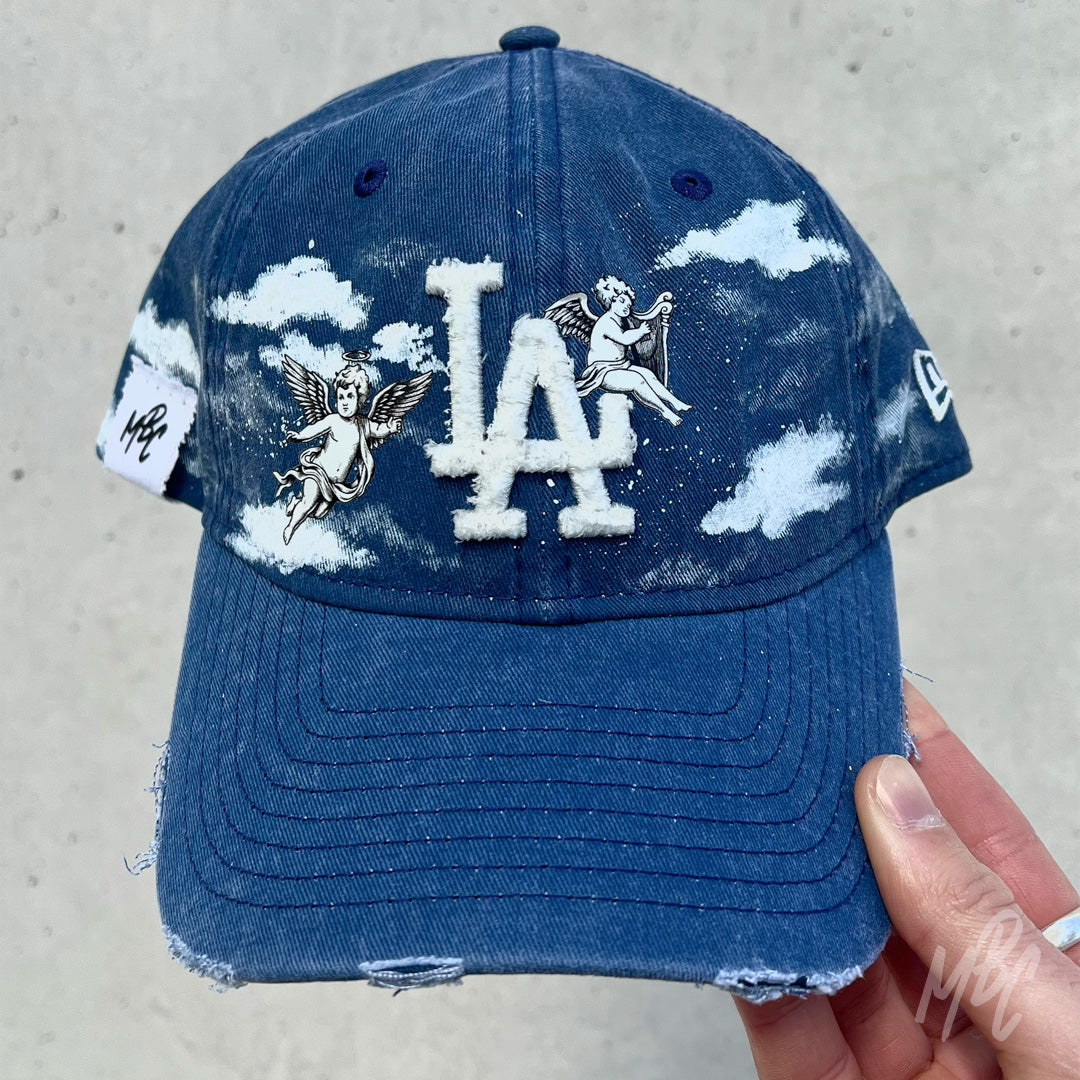 Denim Heaven New Era LA custom cap in blue denim with cherub angel graphics and cloud detailing held outdoors