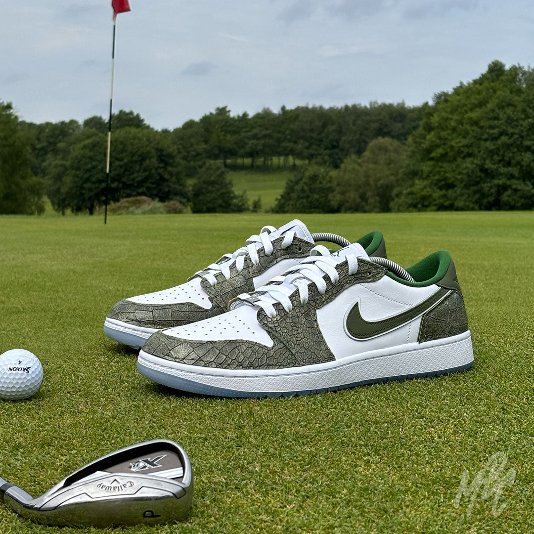 Emerald Reserve Jordan 1 Low Golf custom golf shoes with textured green overlays displayed on a putting green beside a golf ball and iron club