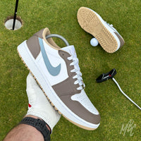 Fairway Fog Jordan 1 Low Golf custom golf shoe held above a putting green beside a golf hole, ball and putter