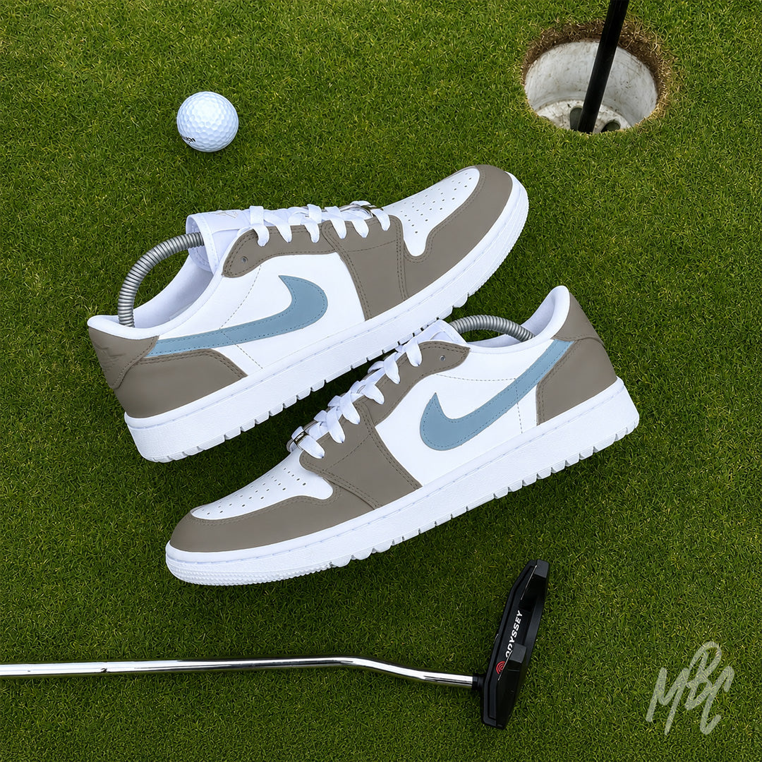 Pair of Fairway Fog Jordan 1 Low Golf custom golf trainers displayed on a putting green with golf ball and putter