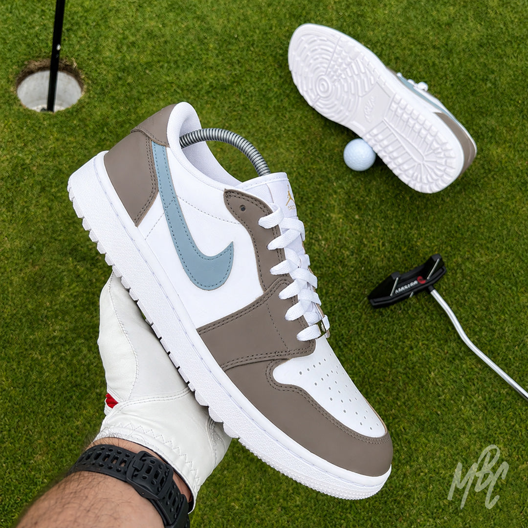 Fairway Fog Jordan 1 Low Golf custom golf shoe held above a putting green beside a golf hole, ball and putter