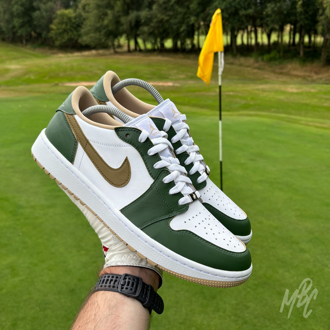 Pair of Fairway Gold custom Jordan 1 Low Golf shoes with hand-painted green and gold colour blocking, held above a golf green beside the pin.