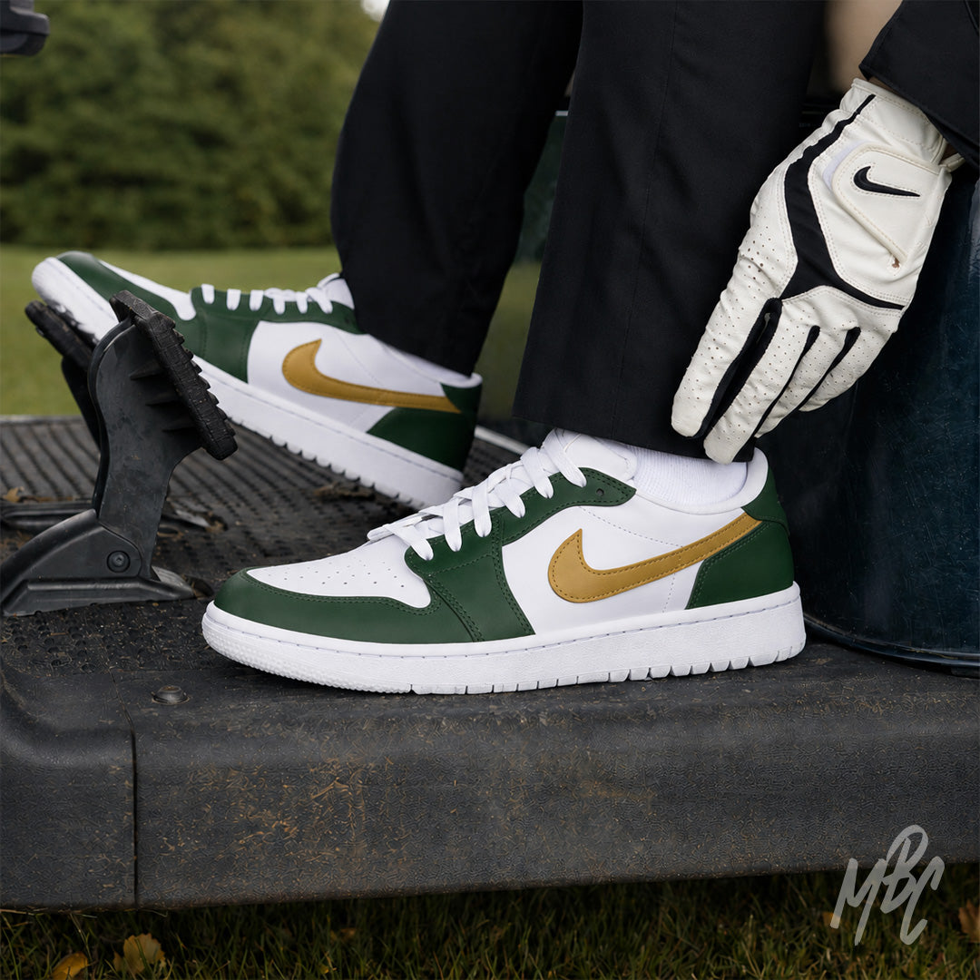 Golfer wearing white Air Jordan 1 Low Golf shoes with dark green overlays and gold Nike Swooshes, seated in a golf cart with a white-and-black golf glove.