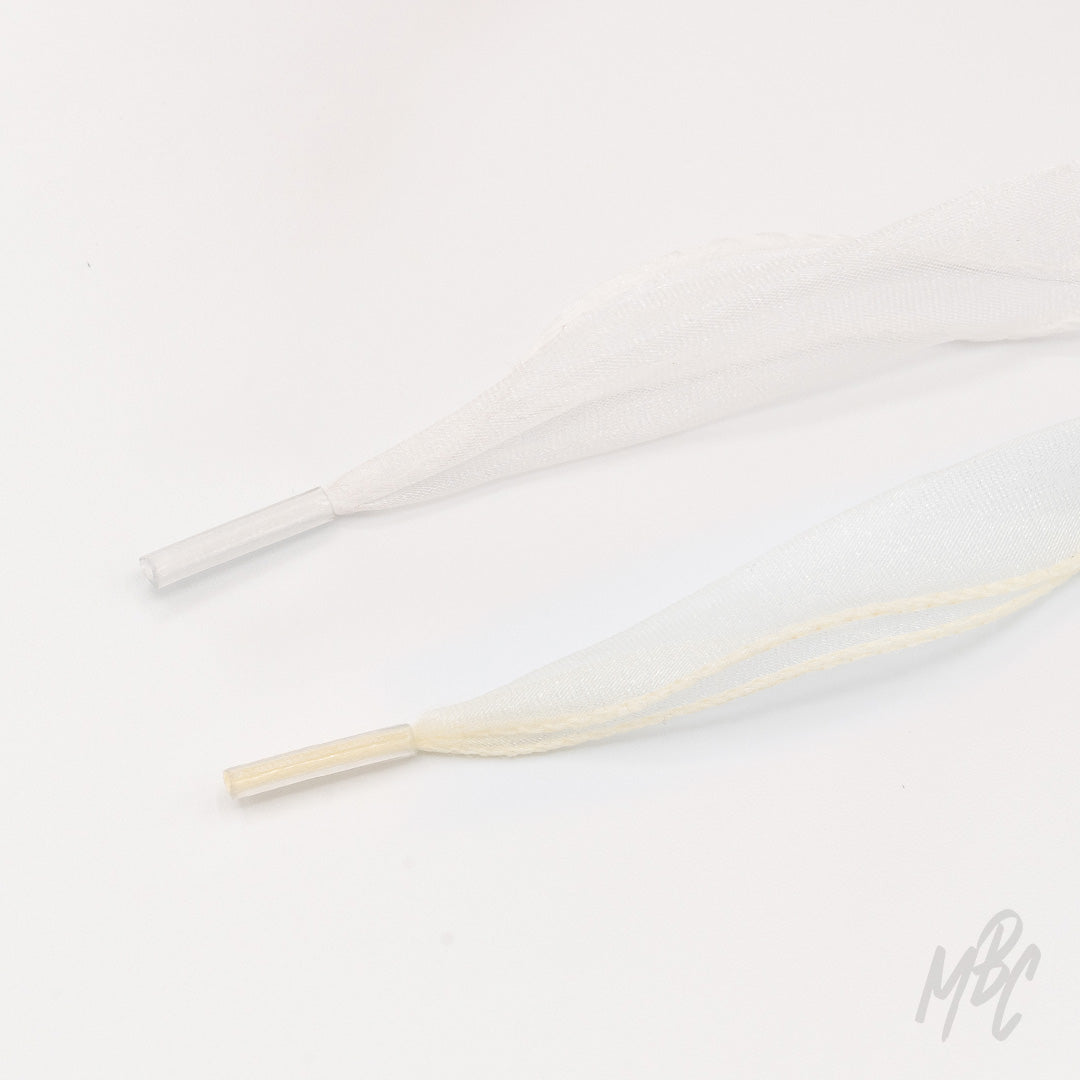 Sheer white and cream fishtail ribbon shoelaces with clear plastic aglets arranged on a white background.