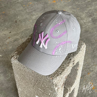 Gradient Swipe custom New Era New York Yankees cap displayed on a concrete block, featuring a pink ombré embroidered NY logo, purple painted swipe graphics and white paint splatter accents.