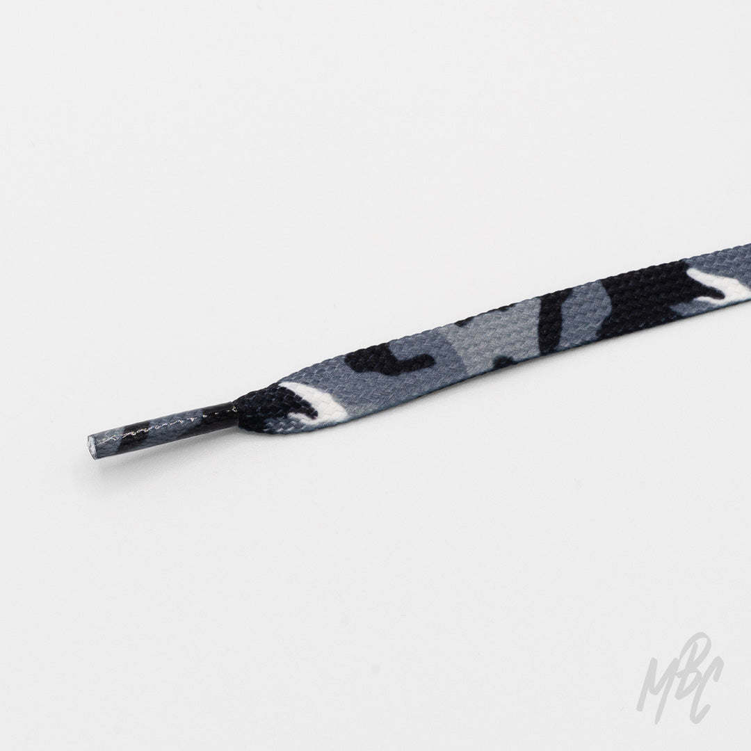 Close-up of a flat grey, black, and white camouflage shoelace with a matching patterned aglet on a white background.