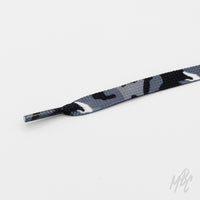 Close-up of a flat grey, black, and white camouflage shoelace with a matching patterned aglet on a white background.