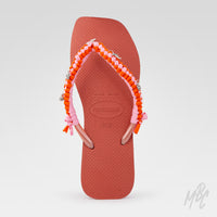 Top view of a peach Havaianas flip-flop customised with pink and orange braided straps and silver beach-themed charms.
