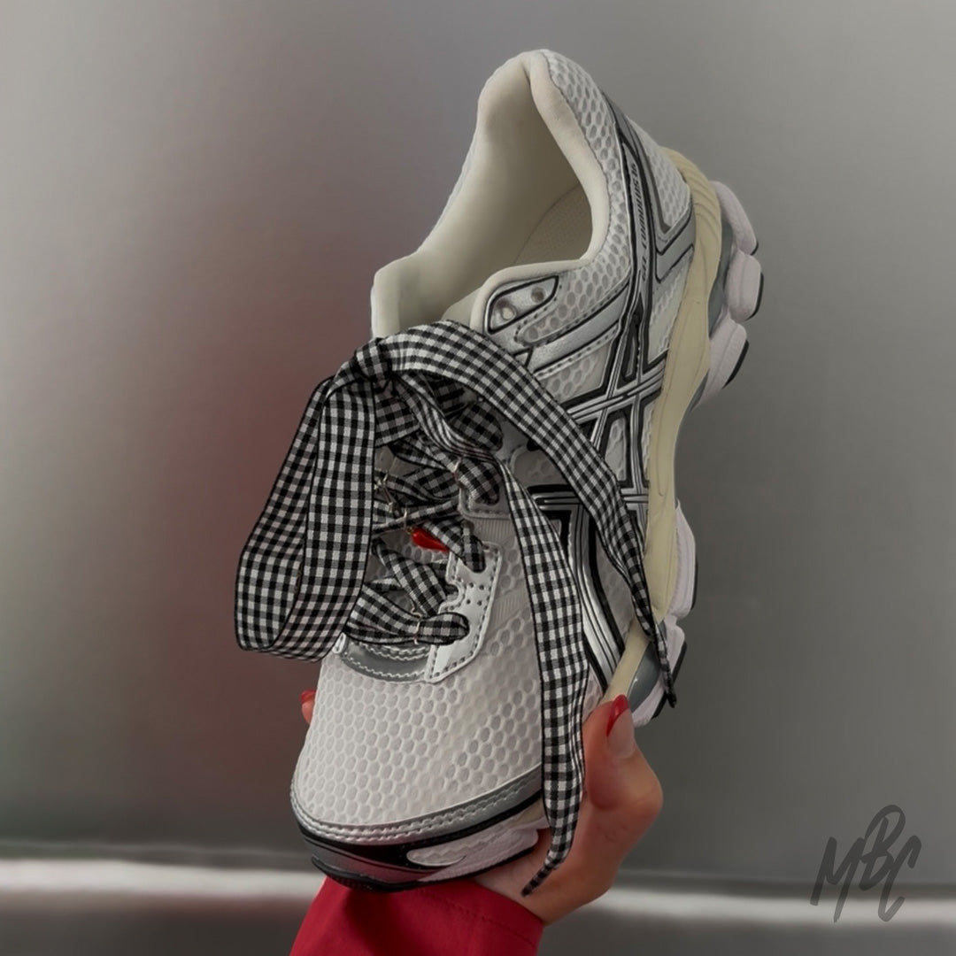 White and silver ASICS trainers with black gingham ribbon laces and decorative sneaker lace accessories