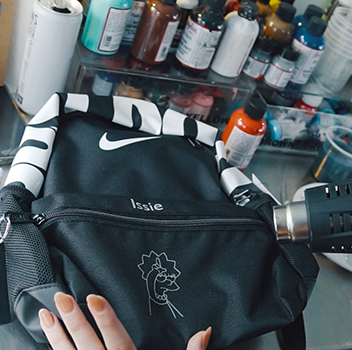 Artist heat gunning an iron on vinyl onto a school bag at the custom back to school bus JD activation