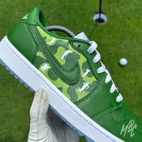 Lines of Play custom Jordan 1 Low Golf shoes featuring hand-painted green camouflage artwork with white golfer silhouettes, photographed on a putting green.