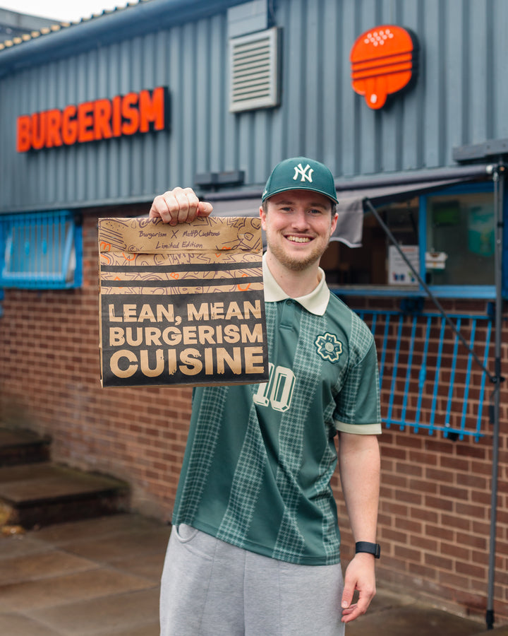 A man stands outside Burgerism holding a limited edition custom paper bag designed by MattB Customs. The bag features bespoke hand-painted artwork created from an original canvas for Burgerism’s exclusive packaging collaboration. Branded packaging by MattB Customs — Manchester-based studio specialising in corporate customisation, brand activations, and bespoke design projects beyond sneakers.