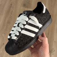 Black and white Adidas Superstar custom sneakers with a textured floral design and wooden background