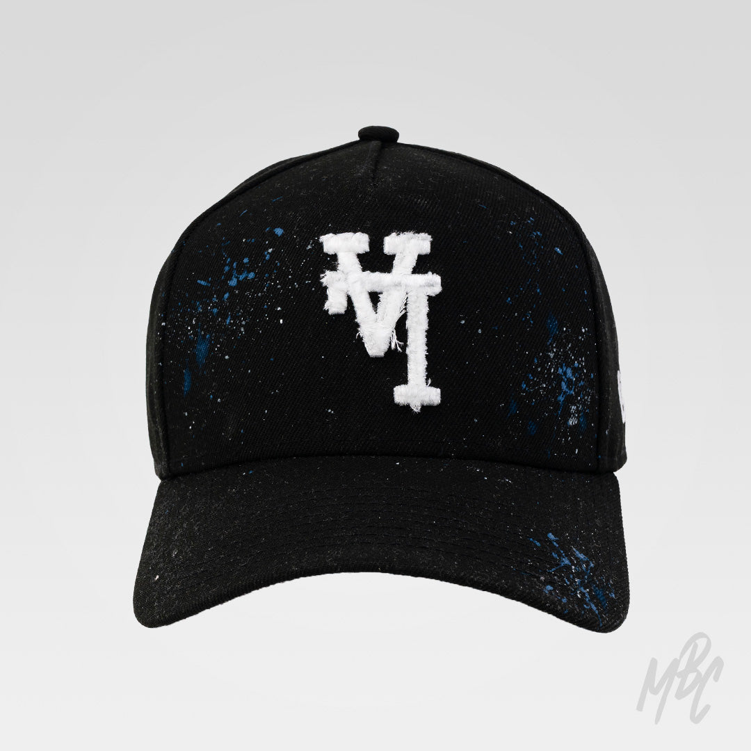 Midnight Canvas custom New Era cap with distressed white embroidered LA logo, hand-painted blue paint splatters and subtle faded detailing on a black baseball cap.