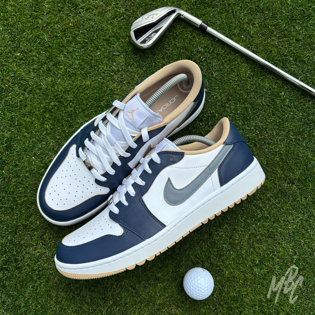 Midnight Tour custom Jordan 1 Low Golf shoes featuring white and grey leather with a navy blue hand painted colourway, displayed on a golf green with a golf club and ball.