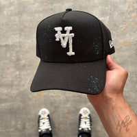 Midnight Canvas custom New Era cap featuring a distressed white embroidered monogram, subtle blue paint splatter detailing and a hand-customised black canvas finish.