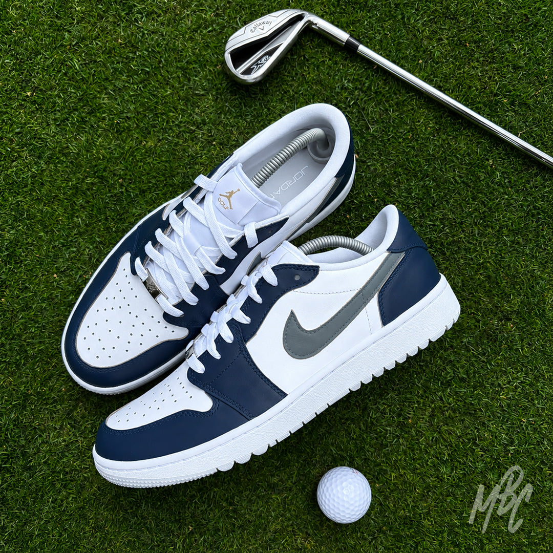 Midnight Tour custom Jordan 1 Low Golf shoes featuring white and grey leather with a navy blue hand painted colourway, displayed on a golf green with a golf club and ball.