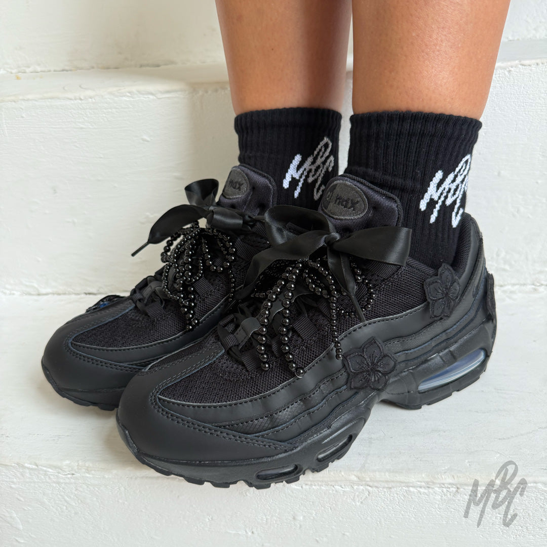 Pair of Midnight Veil custom Nike Air Max 95 trainers featuring black floral appliqués, satin ribbon laces, decorative black bead laces and a sleek all-black finish.