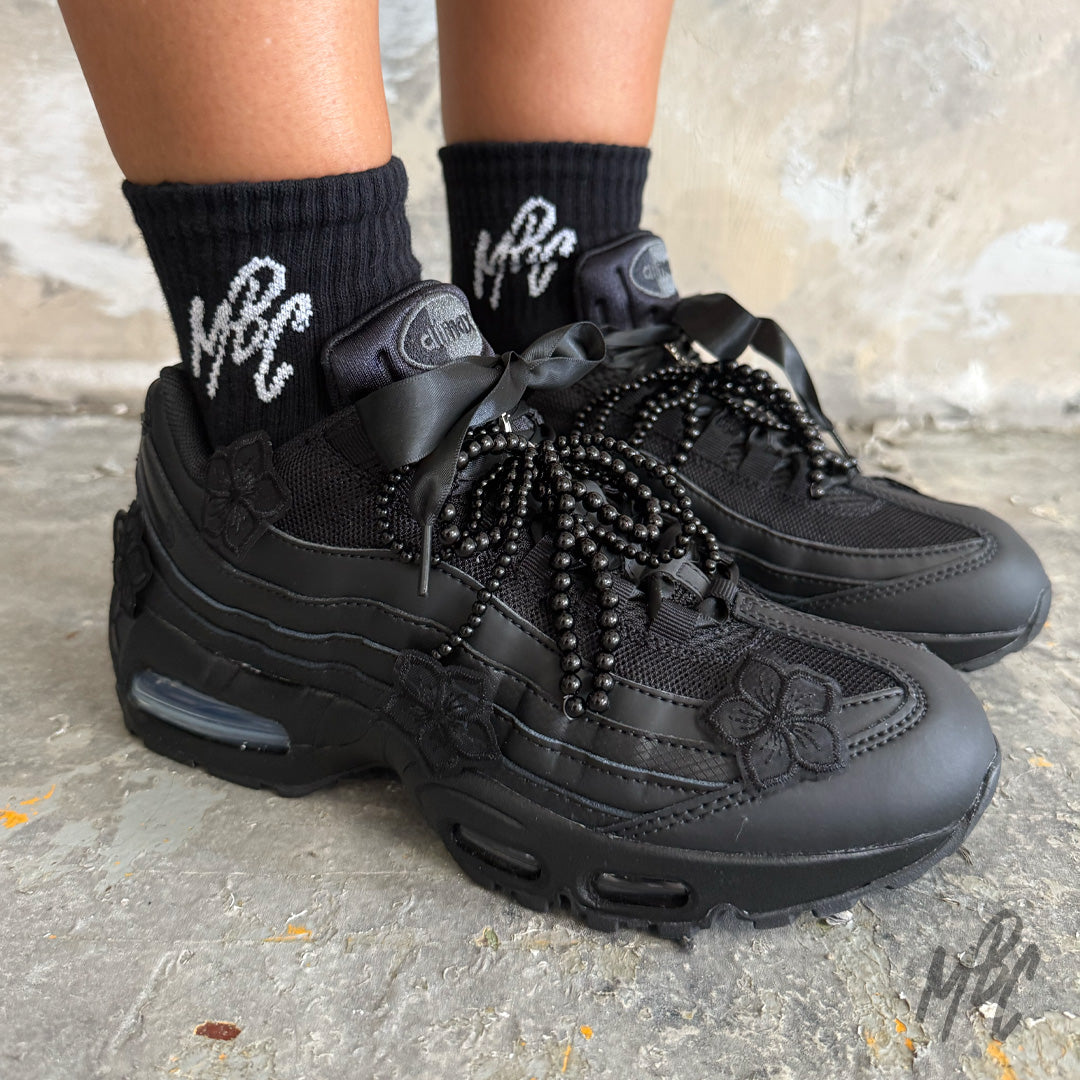 Midnight Veil custom Nike Air Max 95 trainers worn on foot, featuring black floral appliqués, satin ribbon laces, black beaded laces and an all-black hand-customised finish.