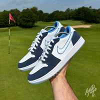 Pair of Navy Suede Jordan 1 Low Golf custom golf shoes held above a golf course green with flagstick in the background