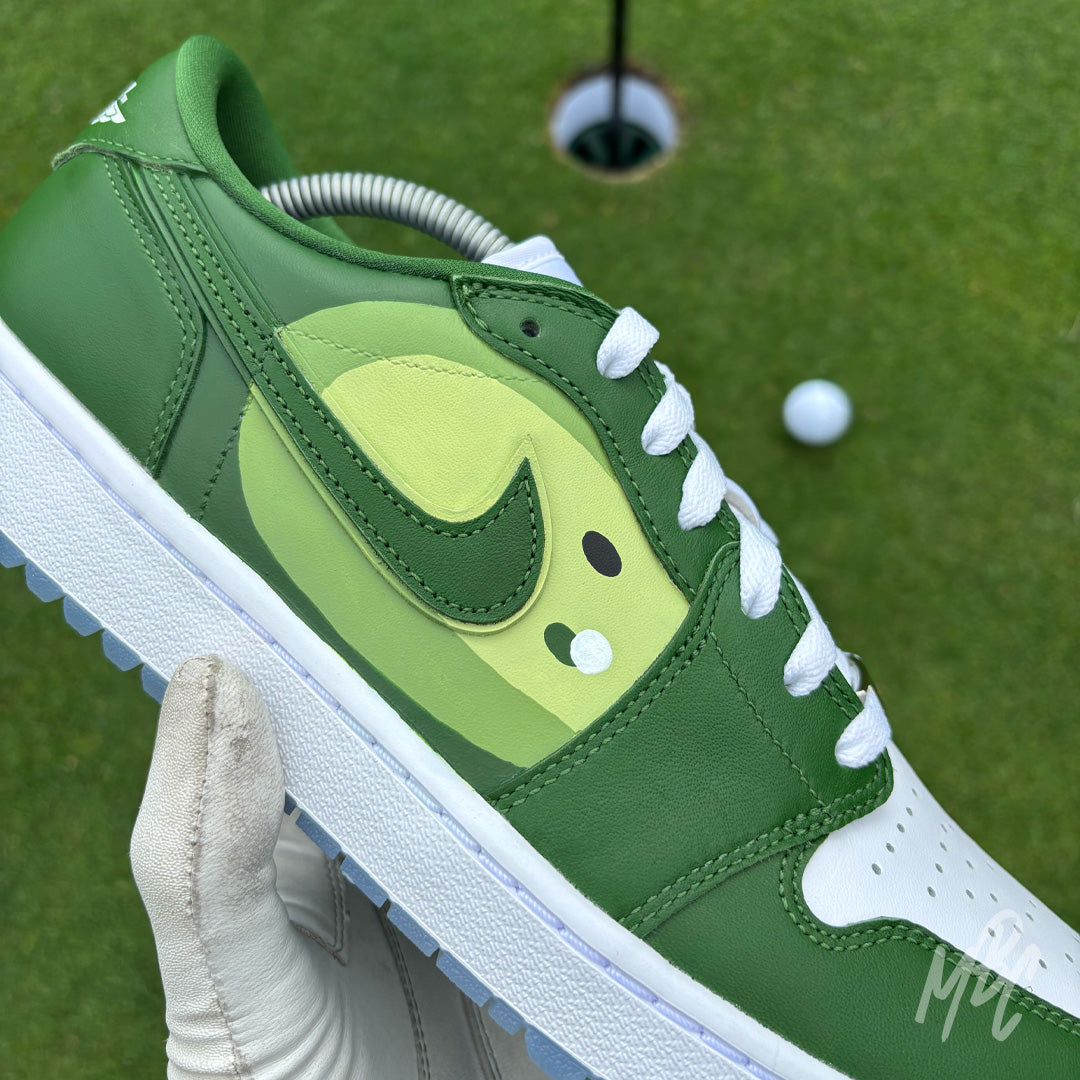 Pin Position custom Jordan 1 Low Golf shoes featuring hand-painted green fairway artwork on white leather, photographed on a putting green with a golf ball and hole.